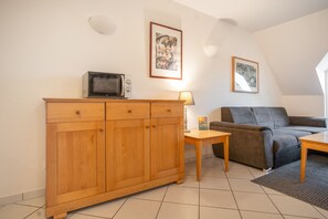 Een woonkamer met een houten kast, een magnetron, een bank, een kleine tafel en twee ingelijste foto's aan de muur.