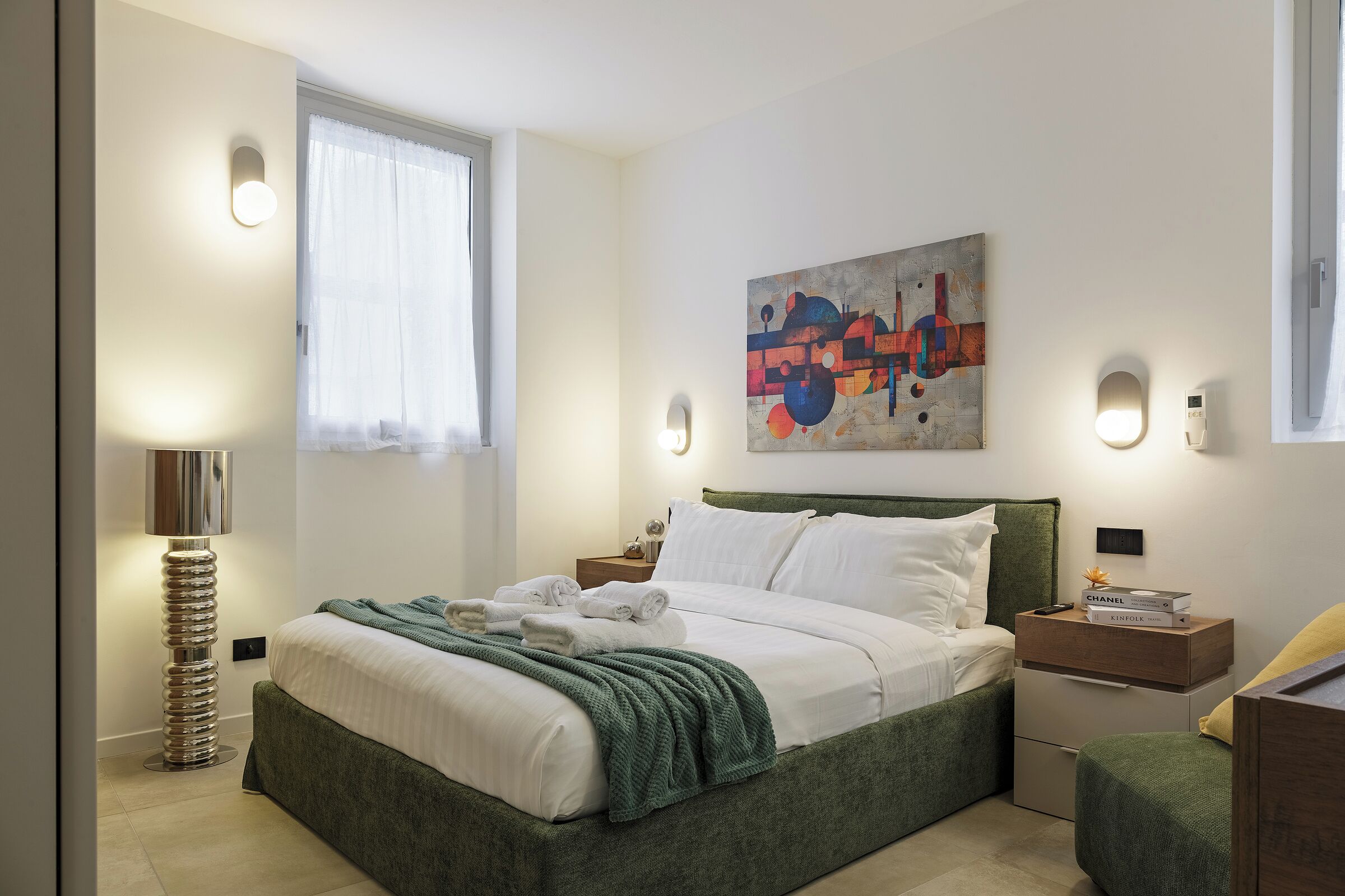 Een moderne slaapkamer met een bed, nachtkastjes, een lamp en een schilderij aan de muur.