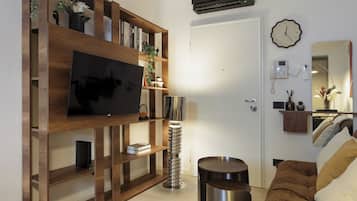 Ein modernes Wohnzimmer mit Flachbildfernseher, Holzböden, einer Lampe, einem runden Tisch und einer Couch.