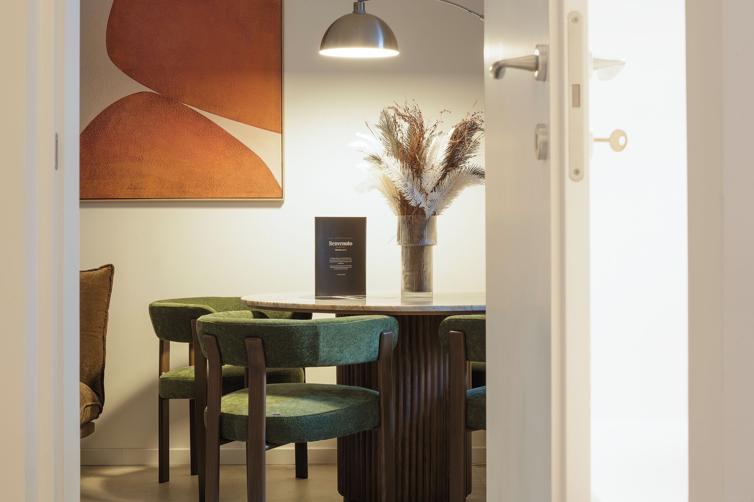 Un coin repas comprenant une table, des chaises, un vase contenant des plantes séchées et une œuvre d’art accrochée au mur.
