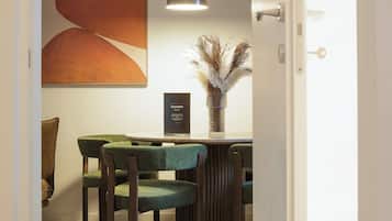 Un coin repas comprenant une table, des chaises, un vase contenant des plantes séchées et une œuvre d’art accrochée au mur.