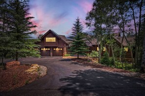 Une cabane en rondins avec un garage, entourée d’arbres et accessible par une allée.