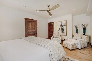 A bedroom with a large bed, a ceiling fan, two doors, a chair, a small table, and a painting on the wall. - Escape to the heart of the Rockies! Luxury 5 bedroom home in Silverthorne! (Silverthorne)