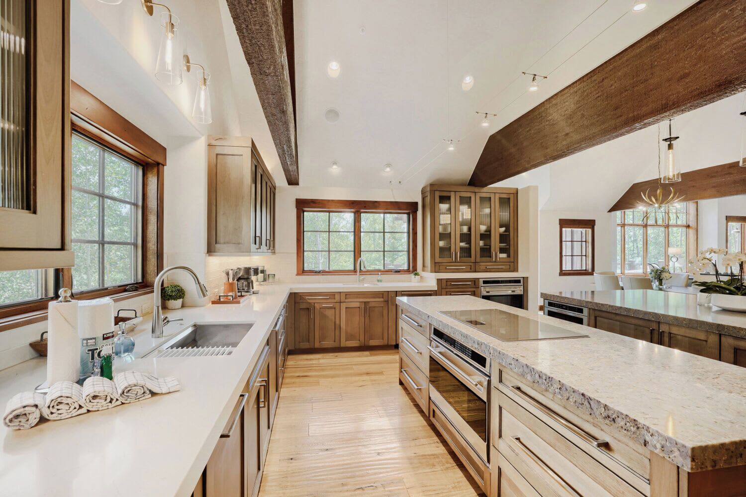 A spacious kitchen with wooden cabinets, a large island, and a view of the outdoors through large windows.