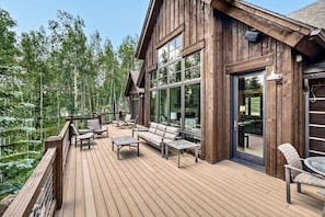 A wooden deck with outdoor furniture, large windows, and a view of a forest. - Escape to the heart of the Rockies! Luxury 5 bedroom home in Silverthorne! (Silverthorne)