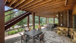 A covered patio with stone flooring, a table and chairs, a grill, and a view of the surrounding greenery. - Escape to the heart of the Rockies! Luxury 5 bedroom home in Silverthorne! (Silverthorne)