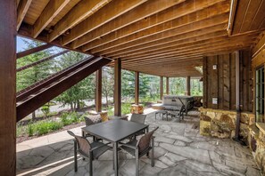 A covered patio with stone flooring, a table and chairs, a grill, and a view of the surrounding greenery. - Escape to the heart of the Rockies! Luxury 5 bedroom home in Silverthorne! (Silverthorne)