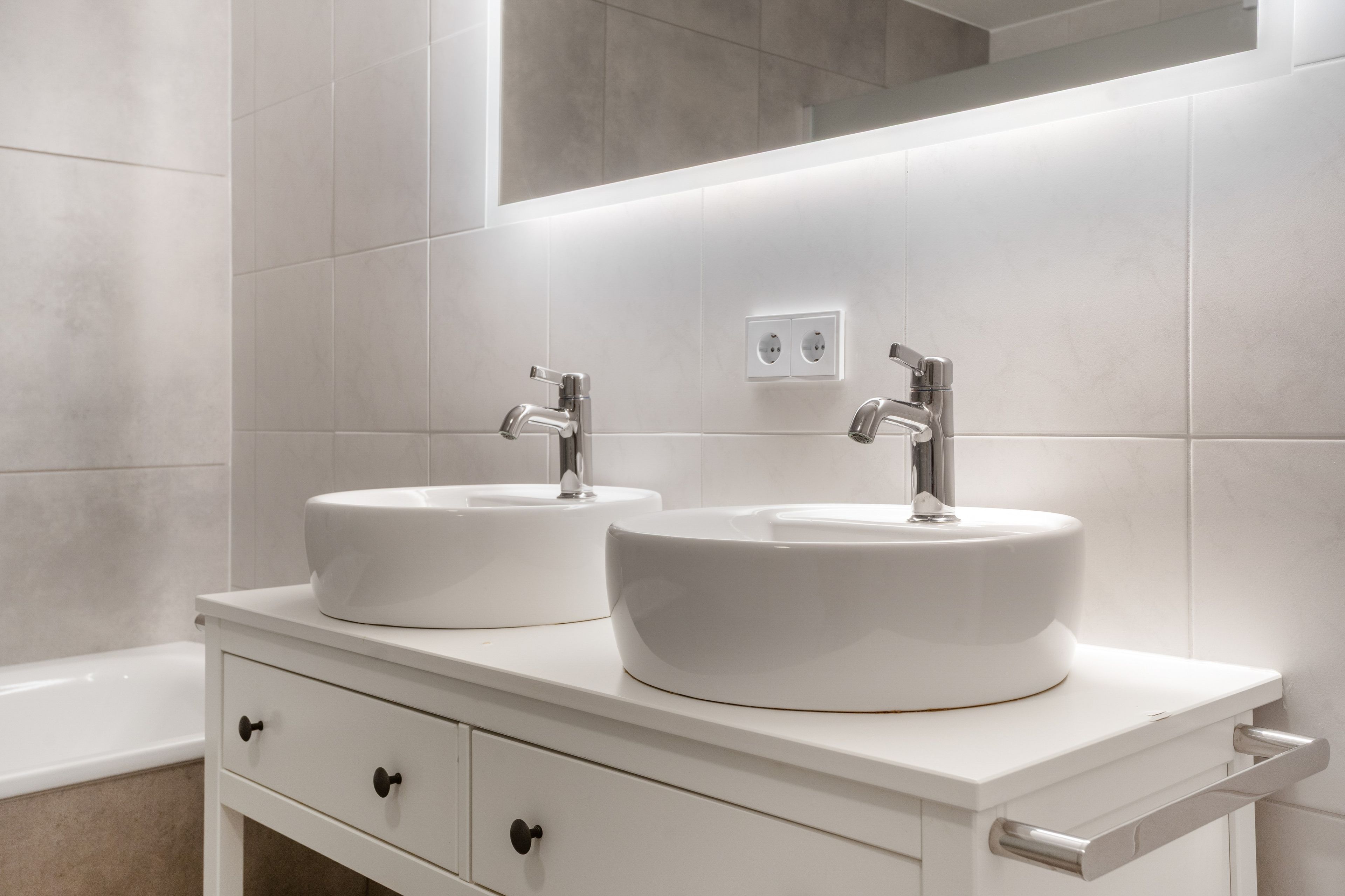 A bathroom with two white sinks, a mirror, and a white vanity with drawers.