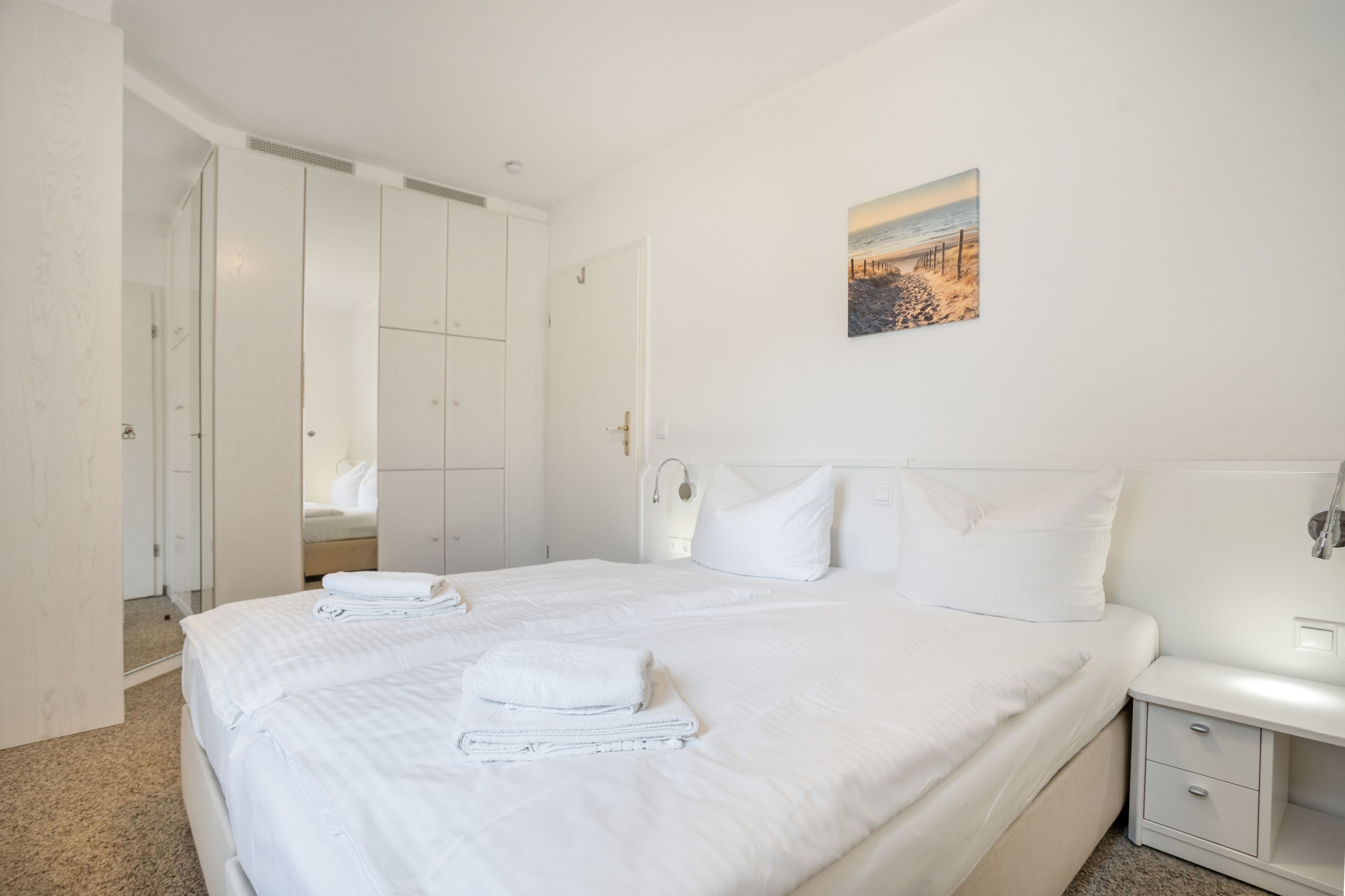 Une chambre d’hôtel avec un grand lit, une table de chevet, une commode et un tableau au mur.