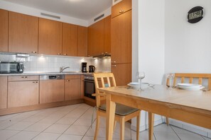 Eine moderne Küche mit Holzausstattung, einem Backofen, einer Kaffeemaschine und einem Esstisch mit Stühlen.