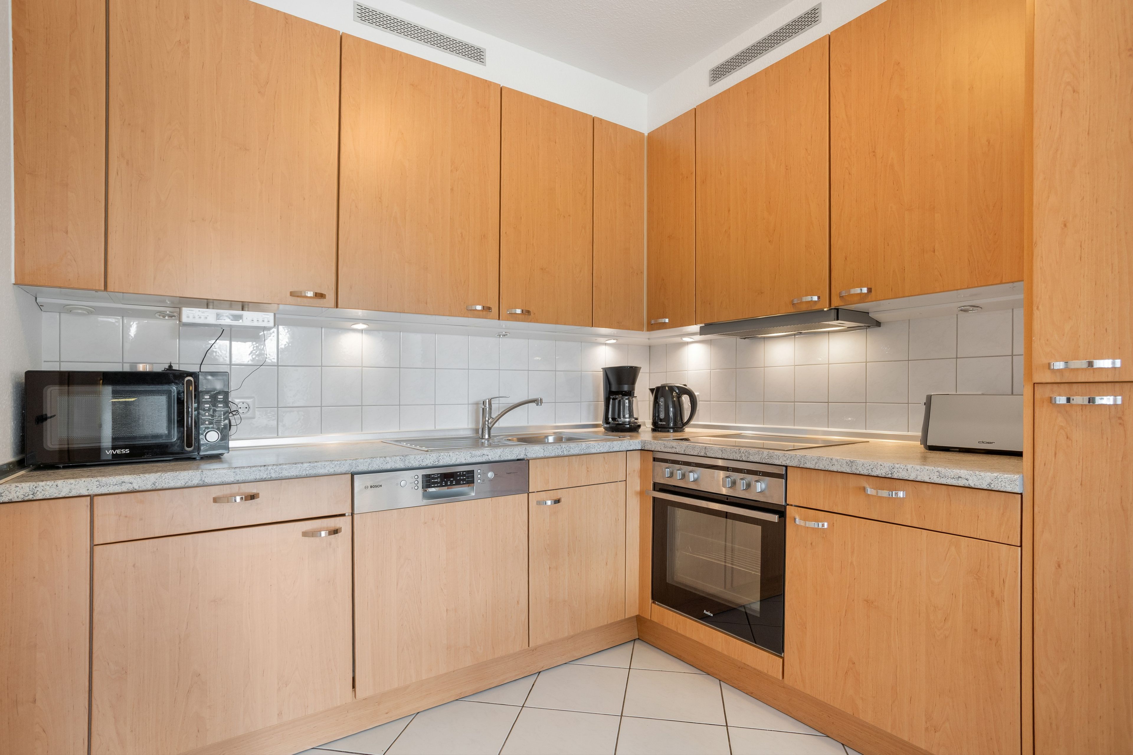 A modern kitchen with wooden cabinets, a microwave, a coffee maker, and a dishwasher.
