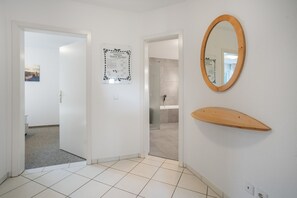 A hotel room with a tiled floor, a wooden shelf, a mirror, and a door leading to a bathroom. - Apartment 'Ava' with Balcony and Wi-Fi (Zempin)