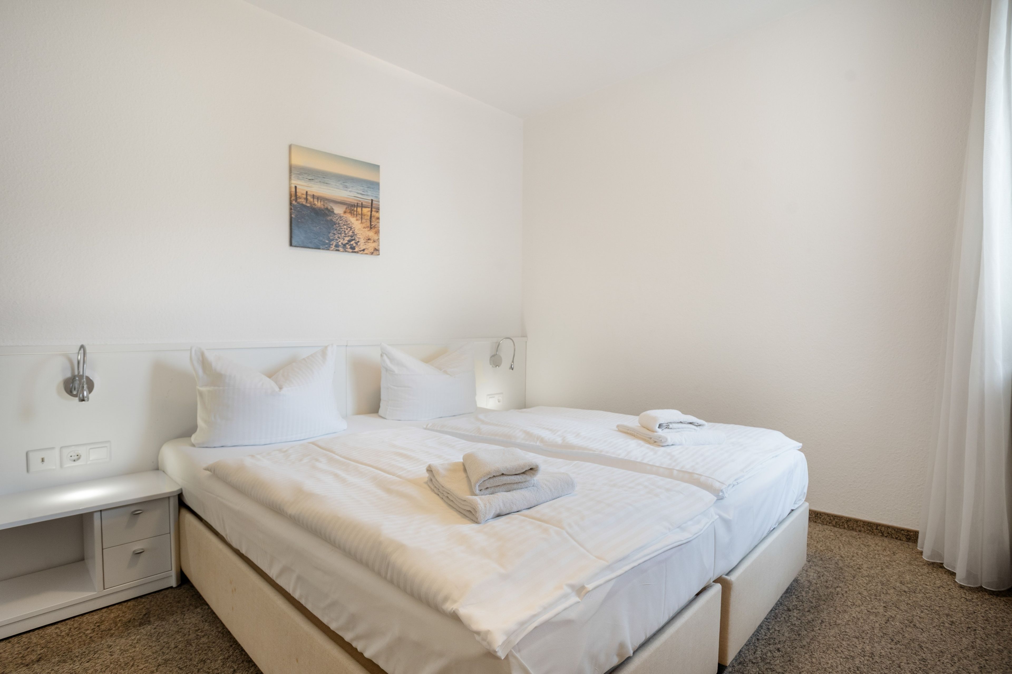 A hotel room with two beds, a nightstand, a wall-mounted picture, and a bathroom with a shower.