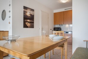 Ein Essbereich mit einem Holztisch, einer Metallschüssel und Weingläsern. Im Hintergrund ist eine Küche mit Holzausbau und einer Mikrowelle zu sehen.