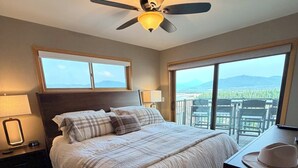 A bedroom with a bed, a ceiling fan, a nightstand, a lamp, a dresser, and a view of the outdoors through large windows. - The best views in Frisco. Highest, corner unit, 600 feet to water's edge. (Frisco)