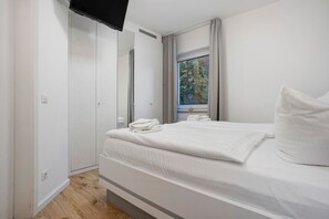 Un dormitorio moderno con cama, ventana con cortinas y televisor de pantalla plana montado en la pared.