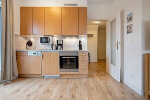 A compact kitchen with wooden cabinets, a microwave, a coffee maker, and a built-in oven. - Apartment "Tine" with Balcony and Beach Chair in Summer (Zempin)