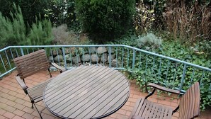Ein runder Holztisch mit Metallstühlen und einem Metallgeländer auf einer Ziegelterrasse.