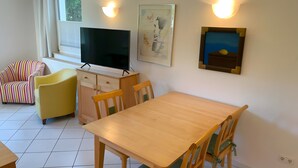 Ein Wohnzimmer mit Fernseher, Esstisch und zwei Stühlen.