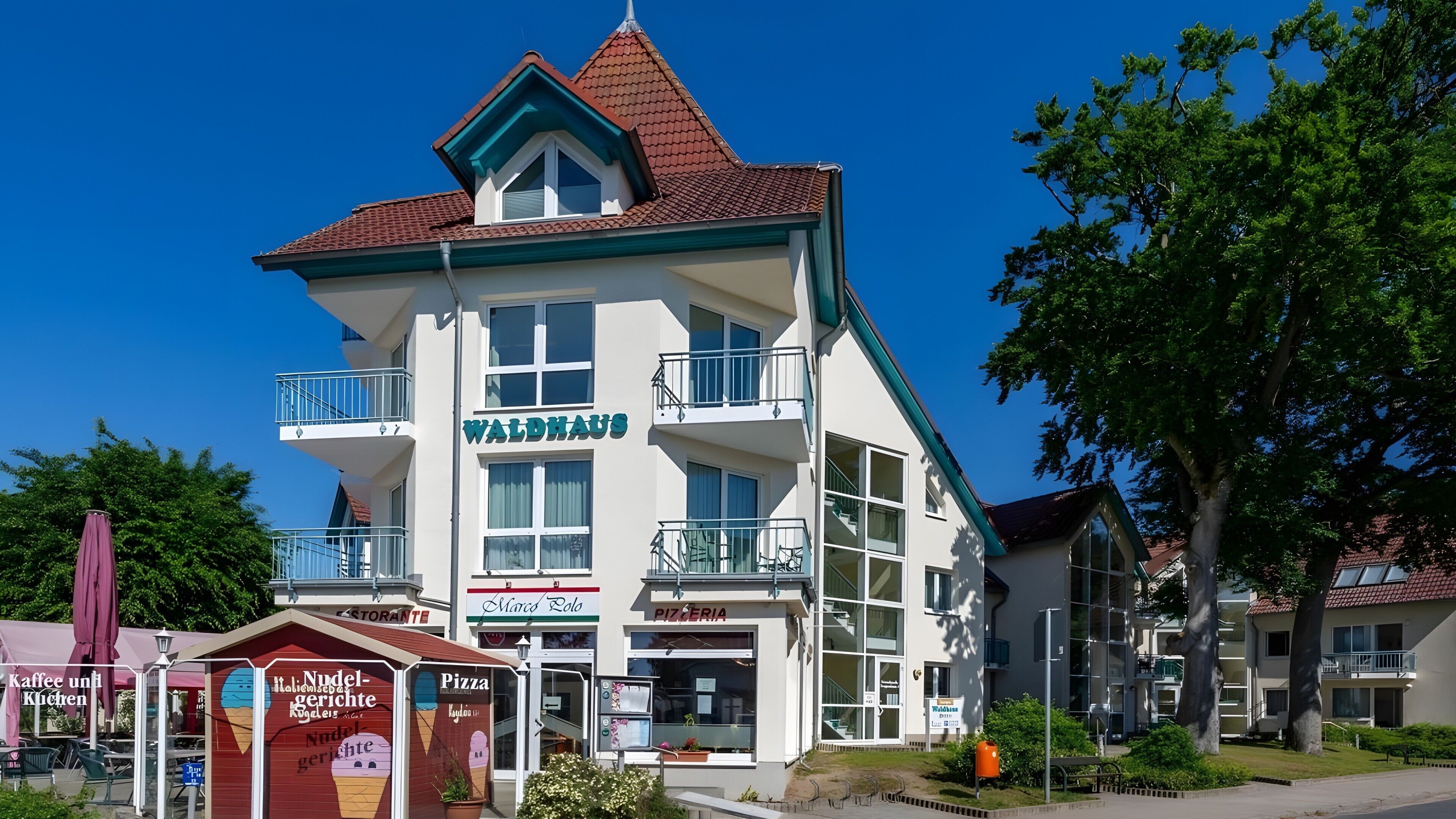 A multi-story building with a sign reading 'WALDHaus' and a 'PIZZERIA' sign below it.