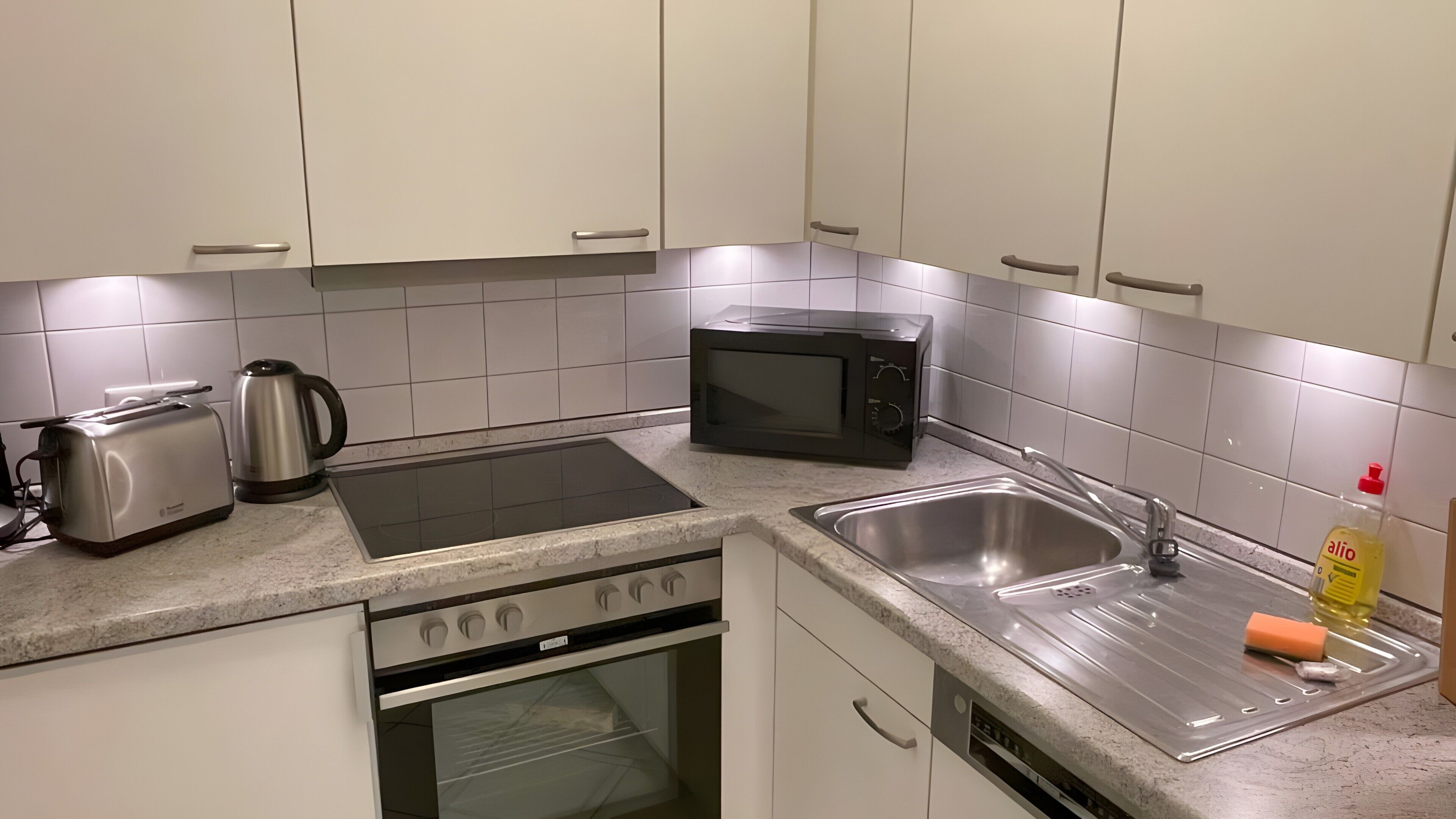 Een keuken met een broodrooster, waterkoker, magnetron, oven en spoelbak.