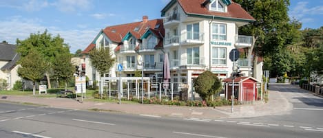 Un immeuble à plusieurs étages, doté d’un toit recouvert de tuiles rouges, de balcons et d’une enseigne indiquant qu’il s’agit d’un restaurant.