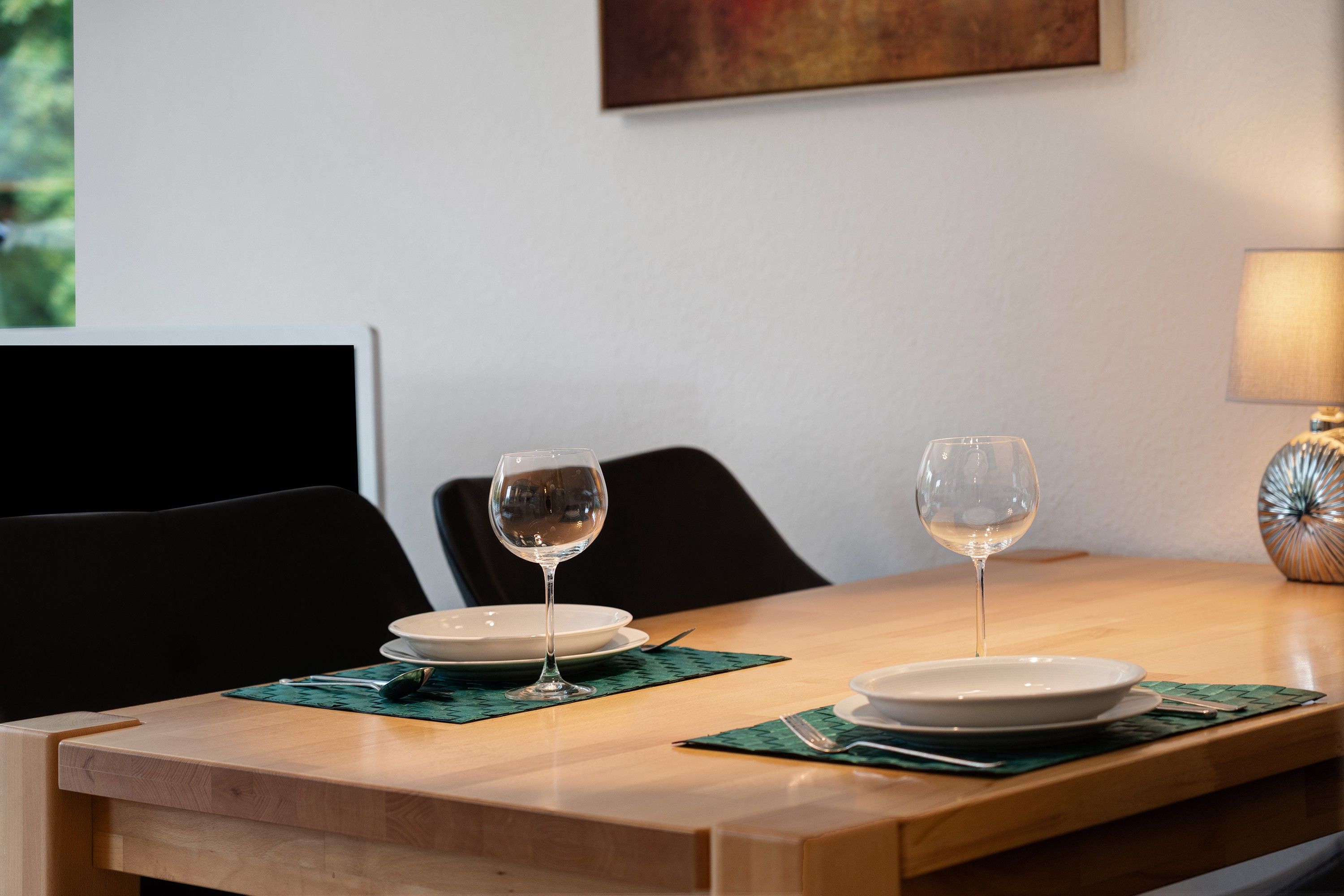 Ett matbord med två vinglas och tallrikar, en lampa och en stol.