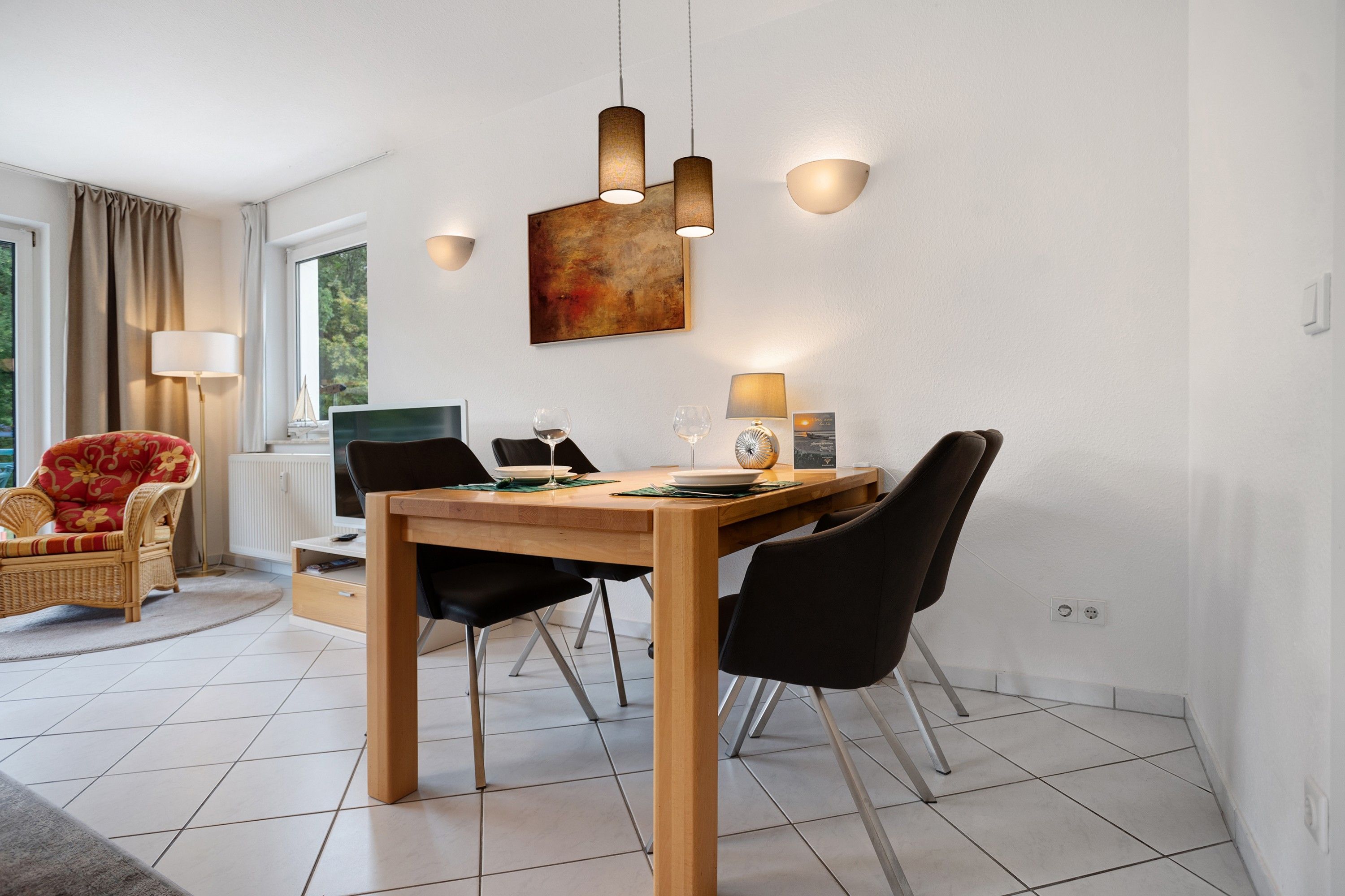 Uma sala de jantar moderna com mesa de madeira, cadeiras pretas e iluminação pendente.