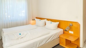 Un letto matrimoniale con lenzuola bianche, due comodini, una lampada da parete e un tavolino.