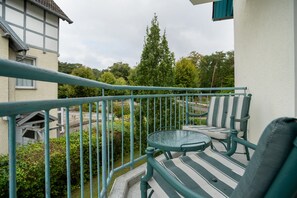Un balcon avec une table et des chaises, donnant sur une rue et des espaces verts.