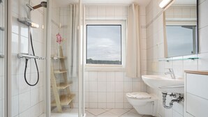 Un baño moderno con cabina de ducha de vidrio, inodoro, lavabo y ventana con vistas al exterior.