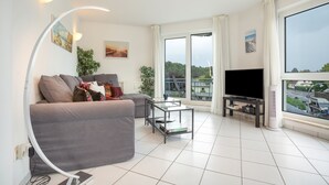 Una sala de estar moderna con un sofá gris, una mesa de centro de vidrio y un televisor de pantalla plana sobre un mueble.