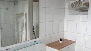 A bathroom with white tiles, a glass shower enclosure, a wooden vanity, and a mirror. - Apartment 'Sonnenblick' with Balcony and Wi-Fi (Zempin)