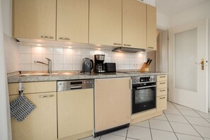 A modern kitchen with wooden cabinets, a stainless steel dishwasher, a coffee maker, and an oven. - Apartment 'Sonnenblick' with Balcony and Wi-Fi (Zempin)