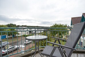 A balcony with a table and chair, overlooking a street with parked cars and buildings. - Apartment 'Sonnenblick' with Balcony and Wi-Fi (Zempin)