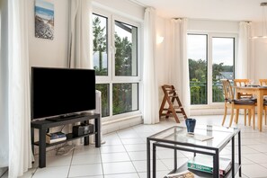 Ein modernes Wohnzimmer mit Flachbildfernseher, Glastisch und Essbereich mit Holzkästen.