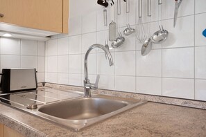 Eine Küche mit Spüle aus Edelstahl, einer eingebauten Dunstabzugshaube und verschiedenen Küchenutensilien, die an der Wand hängen.