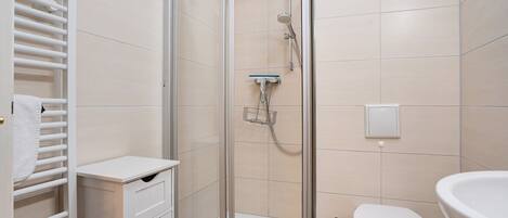 A bathroom with a glass-enclosed shower, a toilet, and a sink.