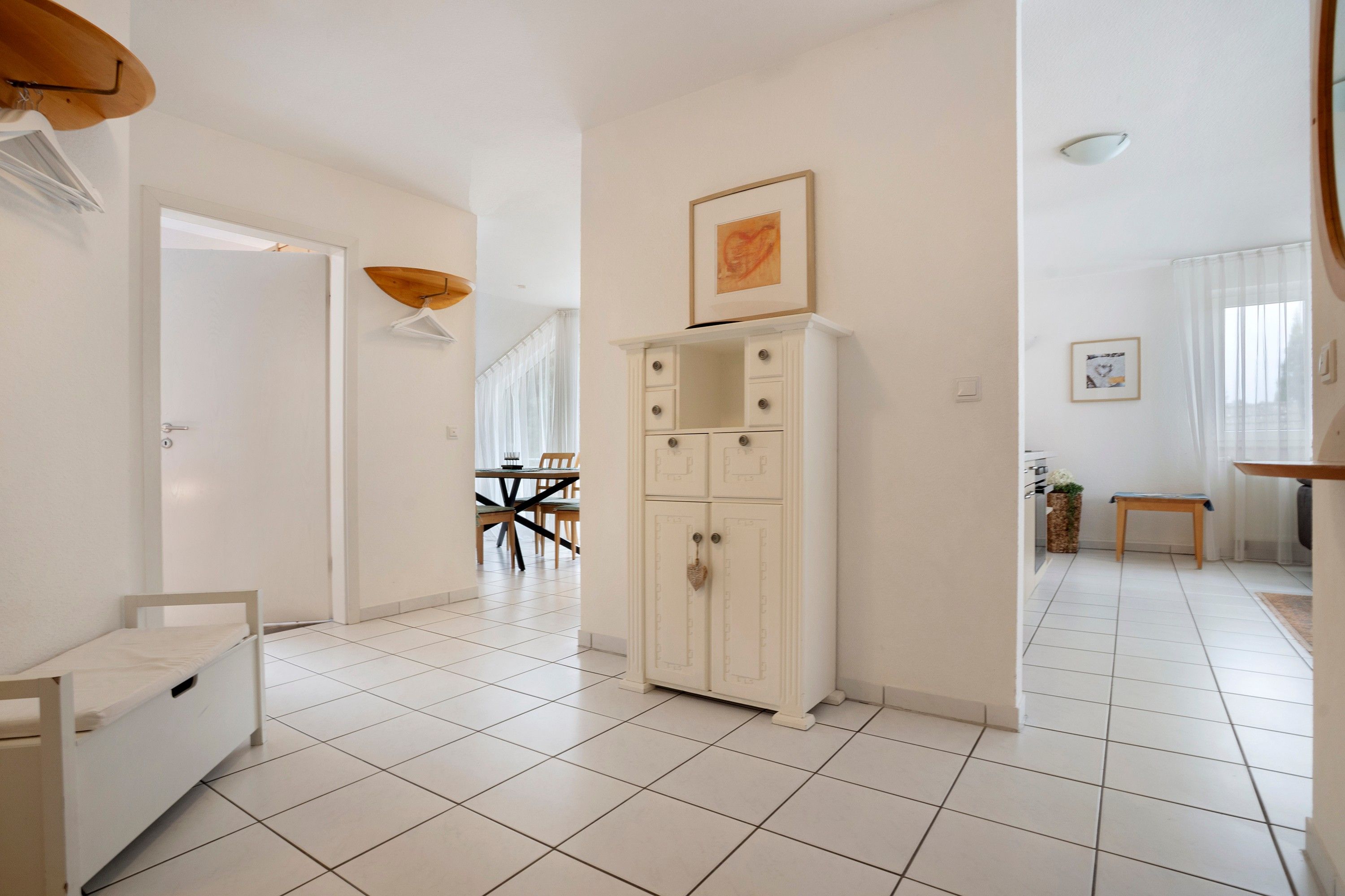 A spacious room with a white cabinet, a dining area with chairs and a table, and a view of the outside through a window.