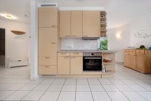 A modern kitchen with light wood cabinets, a built-in oven, and a countertop with a kettle. - Apartment 'Ostseezauber' 75 m², 3 Rooms, Balcony, up to 4 Guests (Zempin)