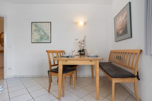 Een eetgedeelte met een houten tafel en stoelen, een vaas met bloemen en een kaart aan de muur.