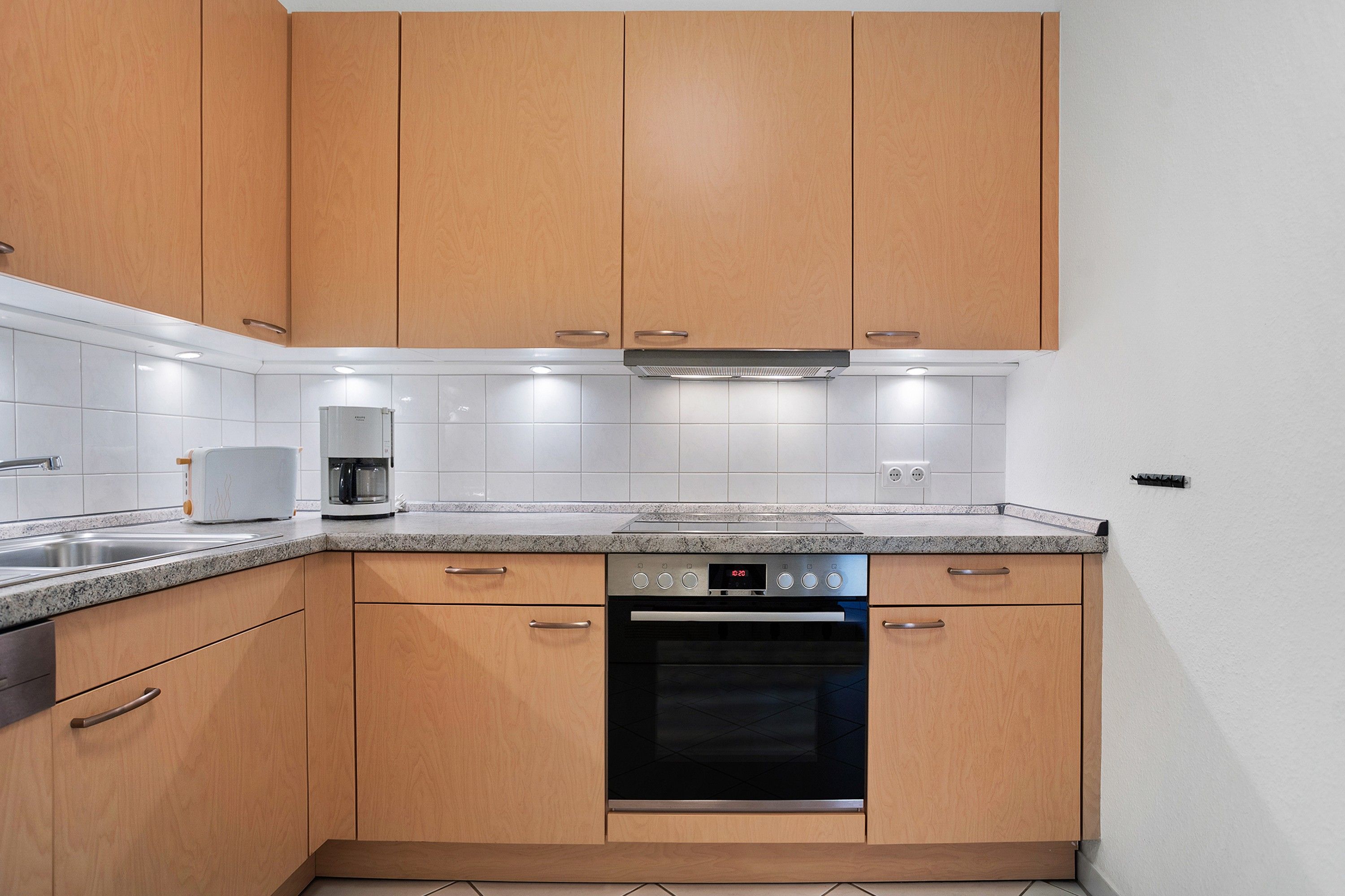 A modern kitchen with wooden cabinets, a built-in oven, and a coffee maker.