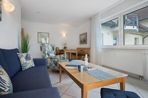 Een woonkamer met een bank, een eettafel, stoelen en uitzicht op buiten.