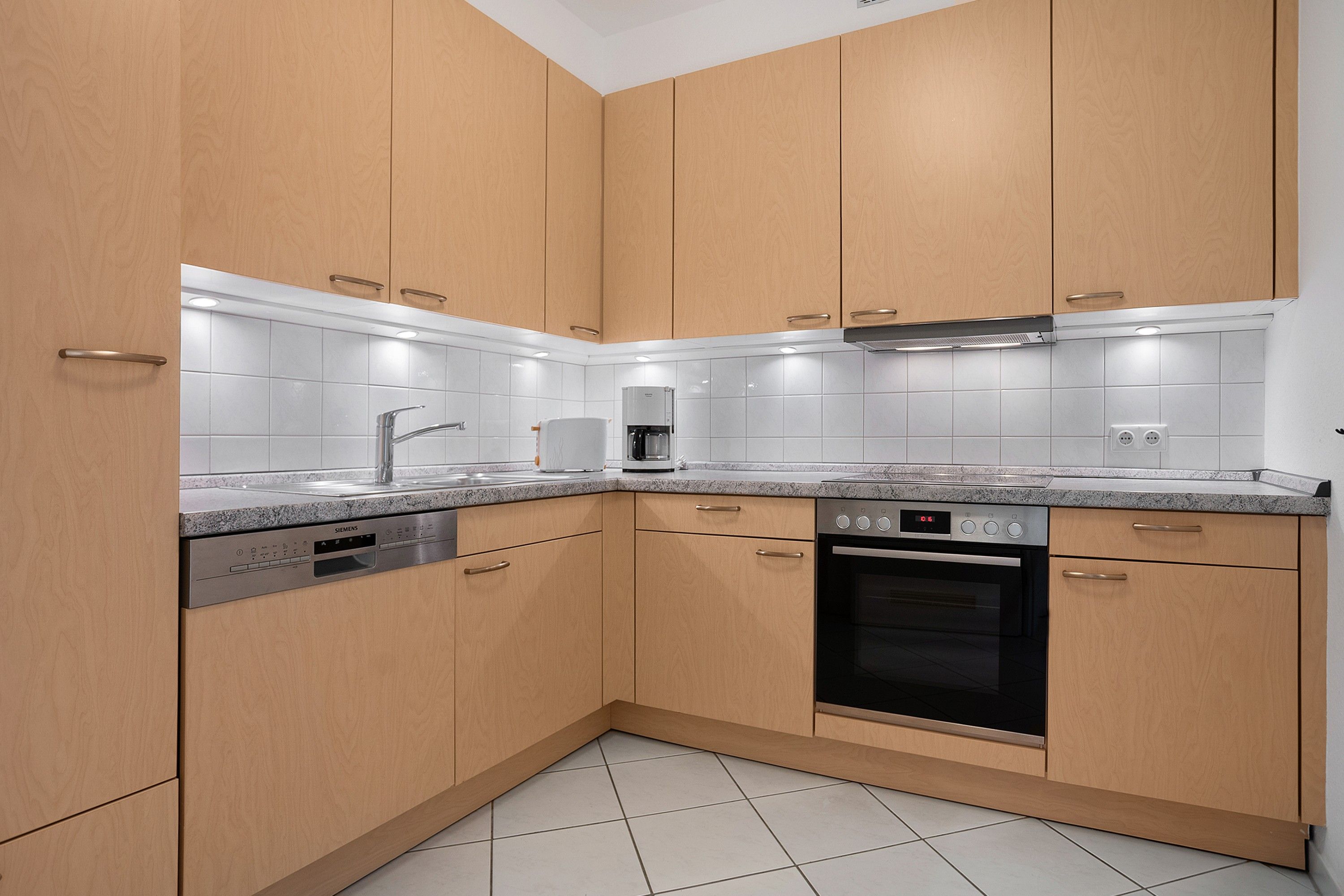 Una cocina moderna con armarios de madera, lavavajillas integrado, cafetera y estufa.