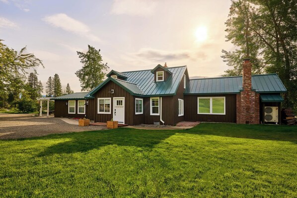 A two-story house with a green metal roof, a brick chimney, and a well-maintained lawn.