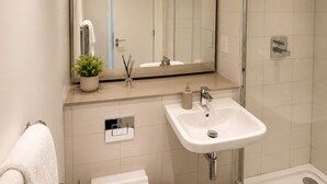 A modern bathroom with a large mirror, white sink, toilet, and shower. - The Nest!! (Salford)