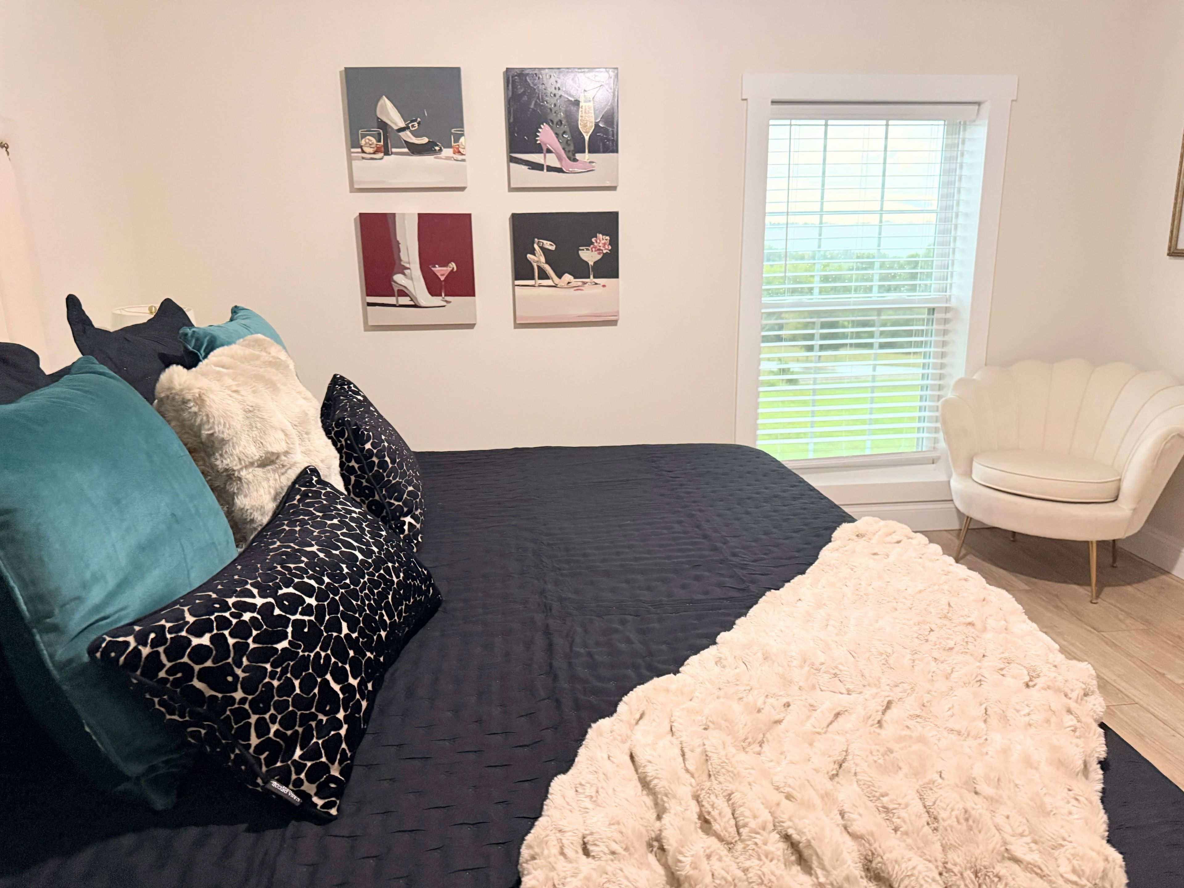 A bedroom with a bed, pillows, a fluffy rug, a window with blinds, and wall art.
