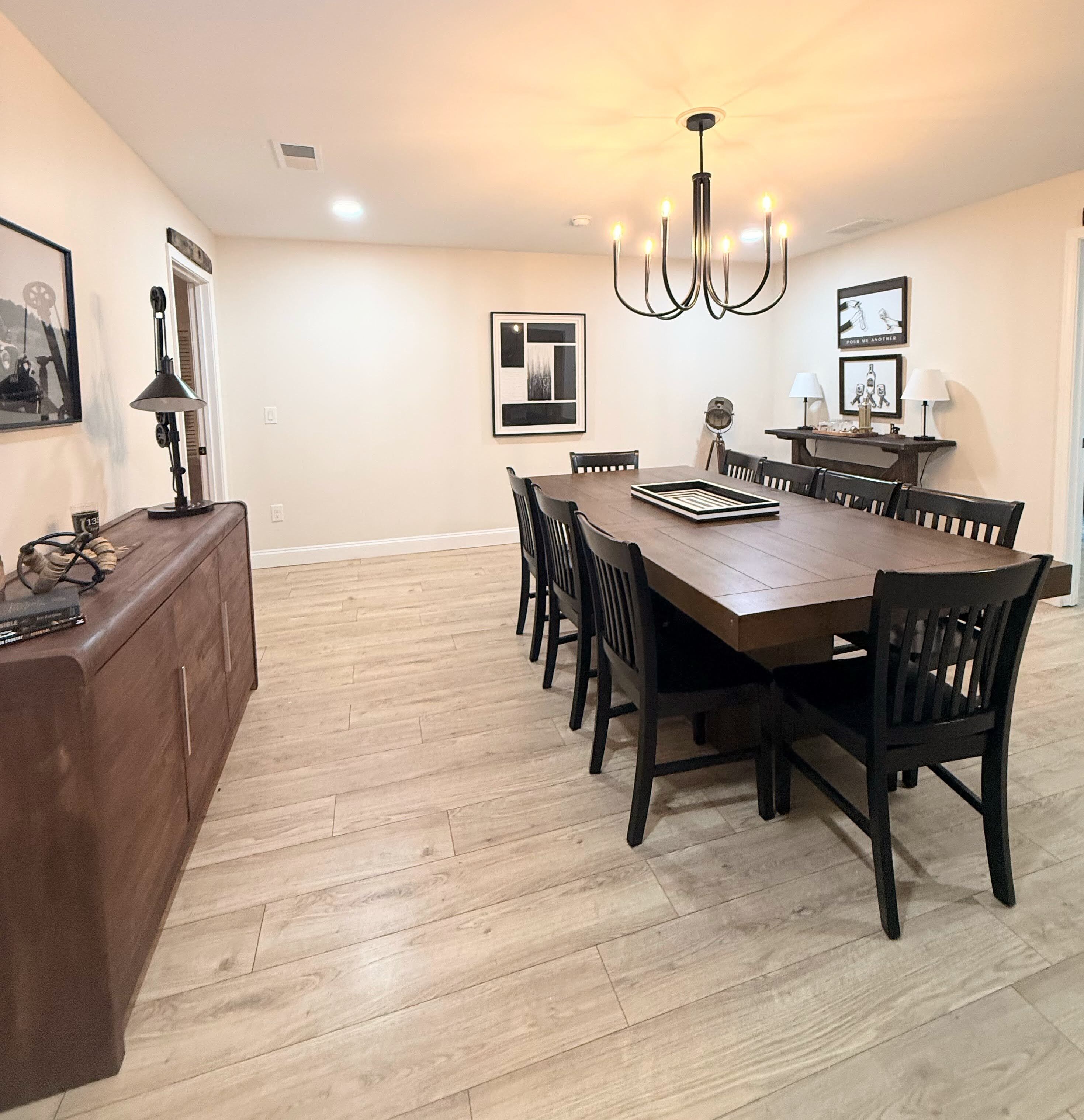 A dining area with a wooden table and chairs, a chandelier, and framed artwork on the walls.