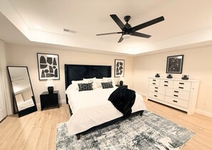A bedroom with a bed, a ceiling fan, a dresser, and artwork on the walls.