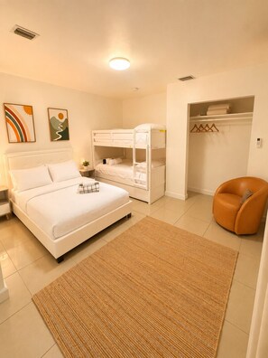 A bedroom with a bed, a bunk bed, a chair, a closet, and a rug.
